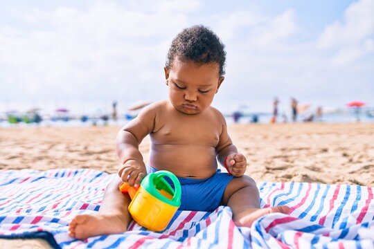 Adorable african american toddler playing with toys sitting on the sand at the beach.