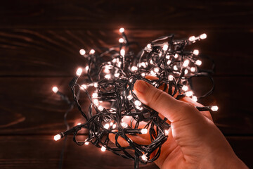 Woman hand holds shining christmas lights garland in a darkness. Glowing LED lightning in a palm. Decorations for winter season holidays Christmas and New Year.