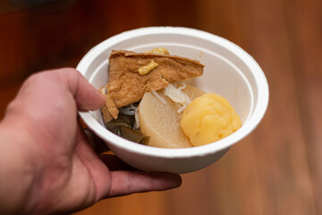 紙皿に盛ったおでんを持つ手。日本文化と食生活、冬の風物詩