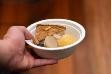 紙皿に盛ったおでんを持つ手。日本文化と食生活、冬の風物詩