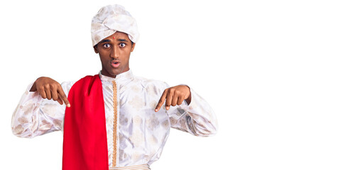 African handsome man wearing tradition sherwani saree clothes pointing down with fingers showing advertisement, surprised face and open mouth