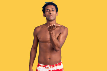 Fototapeta premium African handsome man wearing swimsuit and sunglasses looking at the camera blowing a kiss with hand on air being lovely and sexy. love expression.