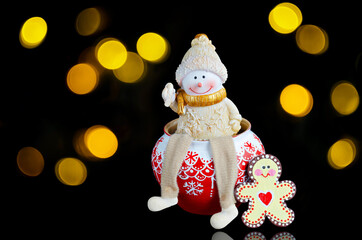 Toy snowman, Christmas pot and wooden gingerbread on black background with bokeh