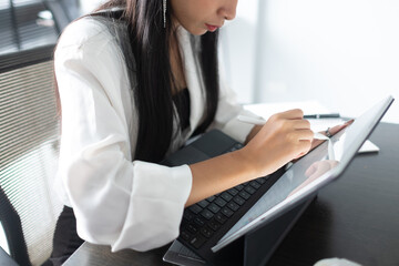 Cropped shot of female hands using digital tablet with stylus on wooden table in office.