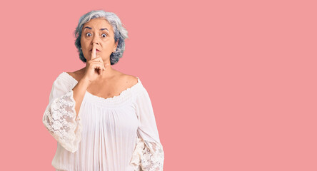 Senior woman with gray hair wearing bohemian style asking to be quiet with finger on lips. silence...