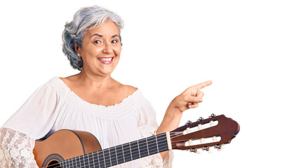Senior woman with gray hair playing classical guitar smiling happy pointing with hand and finger to the side