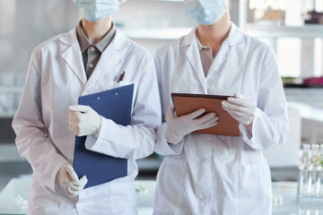 Cropped portrait of two female scientists wearing face mask and holding clipboards while standing in medical laboratory
