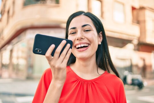 Young latin girl smiling happy sending voice message using smartphone at the city.