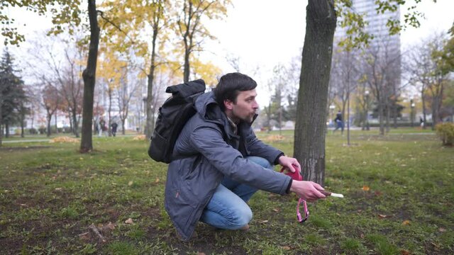 Young Caucasian man looking for a runaway dog in a city park in autumn, holding a bait in his hands and calling for a pet. The theme of people and pets in the city. Finding an obedient husky dog