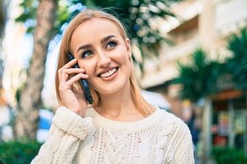 Young blonde girl smiling happy talking on the smartphone at the city.