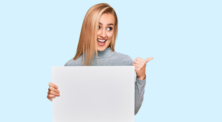 Fototapeta premium Beautiful caucasian woman holding blank empty banner pointing thumb up to the side smiling happy with open mouth