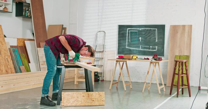 Young carpenter cuts an osb board with a jigsaw. Craftsman's hands in cloth protective gloves. The jigsaw blade cuts precisely.