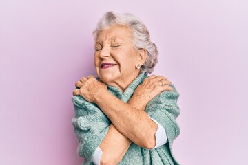Senior grey-haired woman wearing casual clothes hugging oneself happy and positive, smiling confident. self love and self care