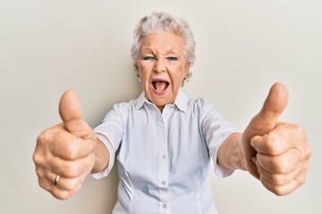 Senior grey-haired woman doing thumbs up positive gesture smiling and laughing hard out loud because funny crazy joke.