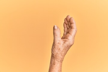 Senior caucasian hand over yellow isolated background picking and taking invisible thing, holding...