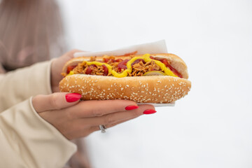 woman holds fresh hot dog in hands, closeup. Hot dog with twhich sausage, grilled onion, mustard, ketchup, pickle cucumbers