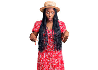 Young african american woman wearing summer hat pointing down with fingers showing advertisement, surprised face and open mouth
