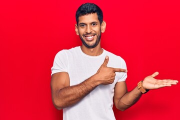 Young latin man wearing casual clothes amazed and smiling to the camera while presenting with hand and pointing with finger.