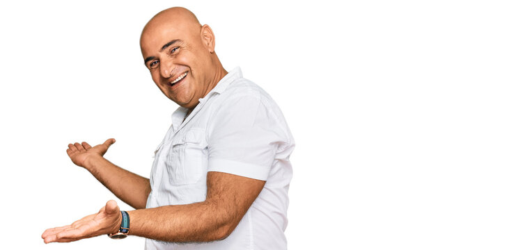 Mature middle east man with mustache wearing casual white shirt inviting to enter smiling natural with open hand