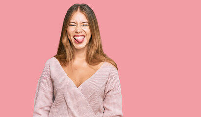 Beautiful blonde woman wearing casual winter pink sweater sticking tongue out happy with funny expression. emotion concept.