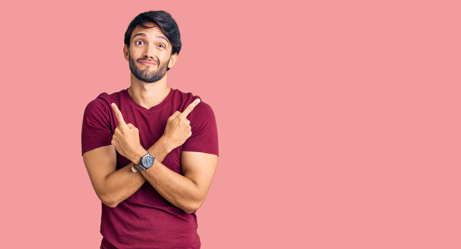 Handsome hispanic man wearing casual clothes pointing to both sides with fingers, different direction disagree