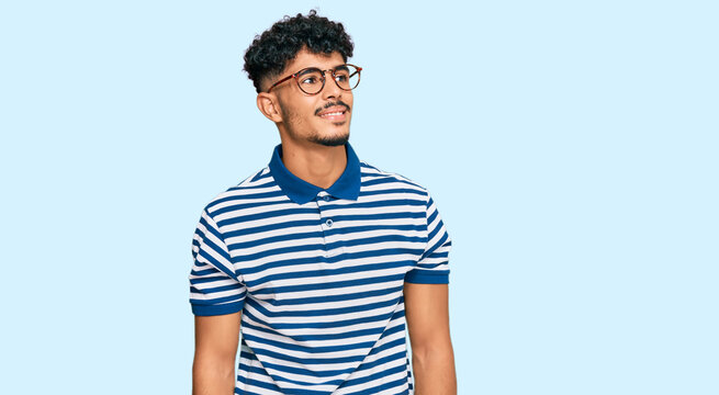 Young arab man wearing casual clothes and glasses looking away to side with smile on face, natural expression. laughing confident.