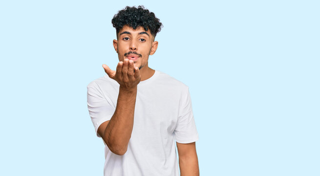 Young arab man wearing casual white t shirt looking at the camera blowing a kiss with hand on air being lovely and sexy. love expression.