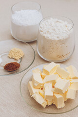 Glass of flour, glass of powdered sugar, pieces of butter and spices on tablecloth. Ingredients for cooking.