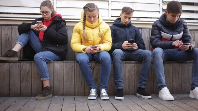 Modern teenagers spending free time outdoor absorbed in online communication. Concept of youth addiction of social networks