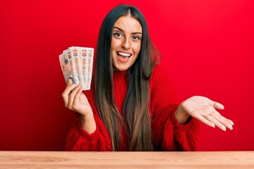 Beautiful hispanic woman holding united kingdom pounds celebrating achievement with happy smile and...