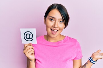 Beautiful young woman with short hair holding paper with email symbol celebrating achievement with happy smile and winner expression with raised hand