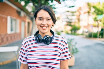 Young latin girl smiling happy listening to music using headphones at the city.