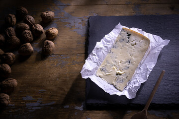 slice of Gorgonzola cheese on black cutting board over wooden table with walnuts. Typical Italian cheese from the Piedmont region