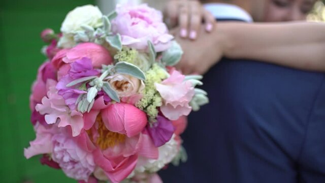 bride hugs the groom, wrapping her arms around his neck, in her hand she has a bouquet, a close-up