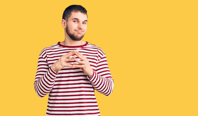 Young handsome man wearing striped sweater hands together and fingers crossed smiling relaxed and cheerful. success and optimistic