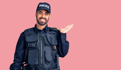 Young hispanic man wearing police uniform smiling cheerful presenting and pointing with palm of...