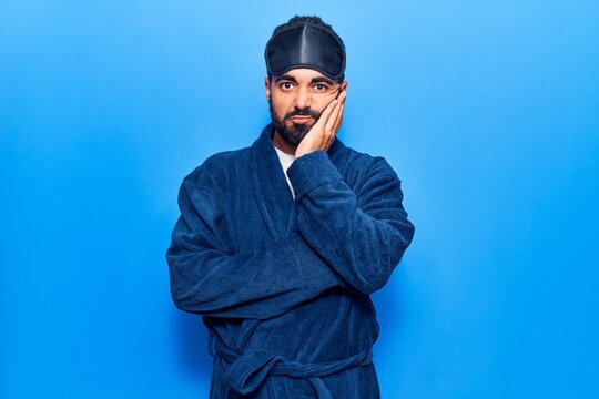 Young hispanic man wearing sleep mask and robe thinking looking tired and bored with depression problems with crossed arms.