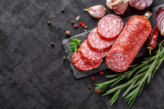 Traditional smoked salami sausage with spices.Salami sausage slices on a black chopping Board. Dark background.