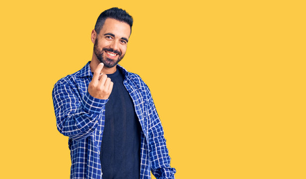 Young hispanic man wearing casual clothes beckoning come here gesture with hand inviting welcoming happy and smiling