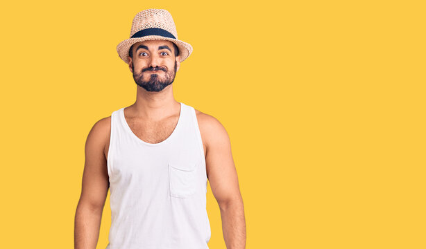 Young hispanic man wearing casual summer hat puffing cheeks with funny face. mouth inflated with air, crazy expression.