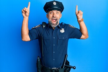 Middle age handsome man wearing police uniform smiling amazed and surprised and pointing up with...