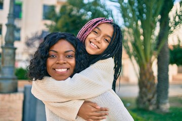 Beautiful african american mother giving daughter piggyback ride smiling happy at the park.