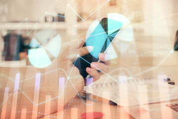 Double exposure of man's hands holding and using a digital device and forex graph drawing. Financial market concept.