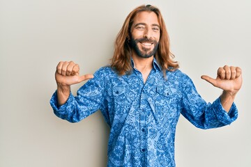 Attractive man with long hair and beard wearing 80s disco style shirt looking confident with smile...