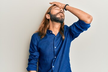 Attractive man with long hair and beard wearing casual clothes surprised with hand on head for mistake, remember error. forgot, bad memory concept.