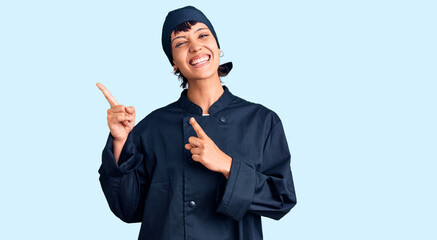 Young brunette woman with short hair wearing professional cook uniform smiling and looking at the camera pointing with two hands and fingers to the side.