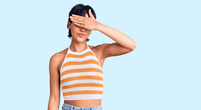 Young brunette woman with short hair wearing casual clothes covering eyes with hand, looking serious and sad. sightless, hiding and rejection concept