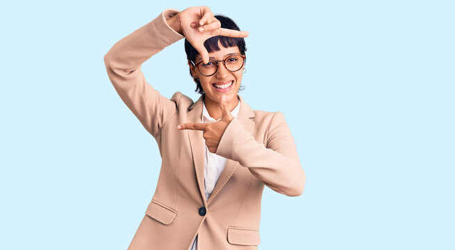 Young brunette woman with short hair wearing business jacket and glasses smiling making frame with hands and fingers with happy face. creativity and photography concept.