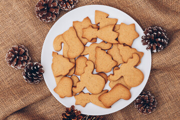 Obraz na płótnie Canvas Tasty Christmas gingerbread cookies on the white plate on a sackcloth.