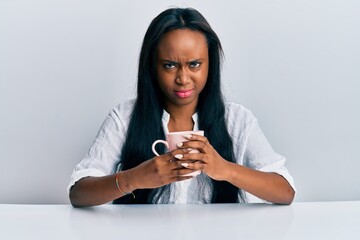 Young african woman drinking a cup coffee skeptic and nervous, frowning upset because of problem....